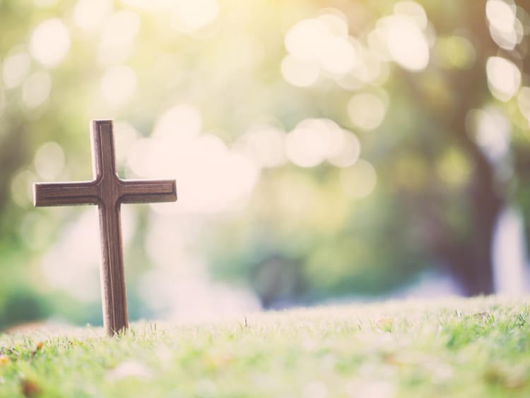 A cross stands alone in an empty grass field