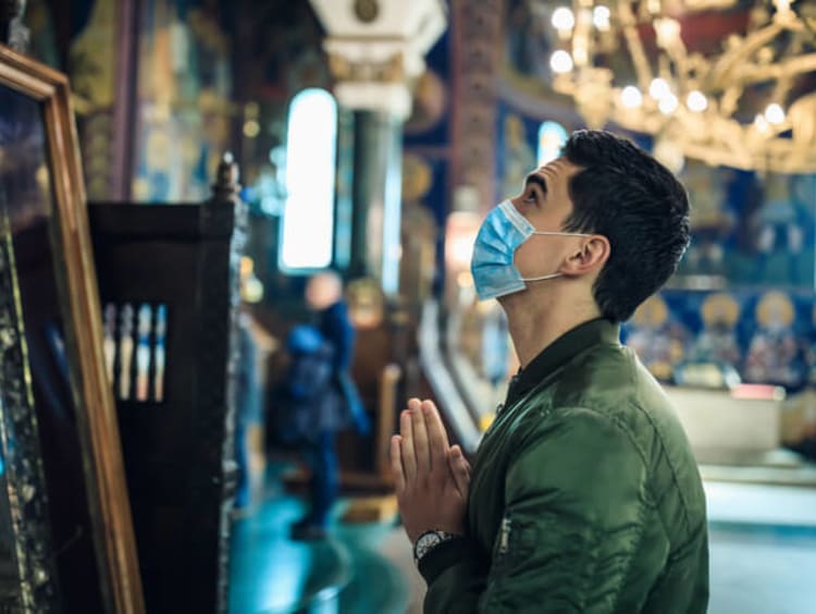 Man has mask on looking up and is praying