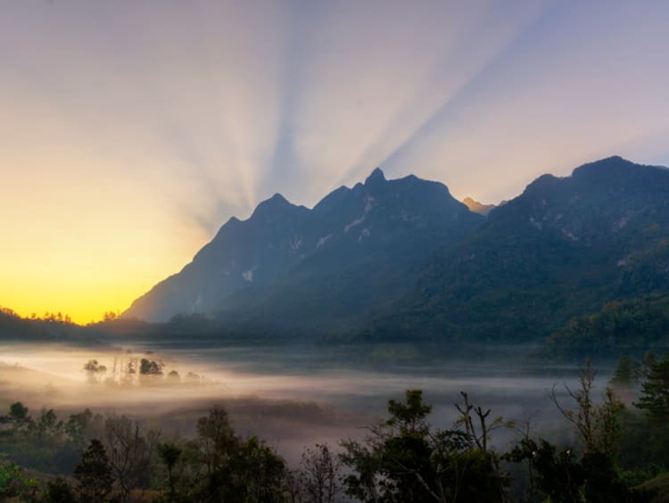 The sun rises behind a mountain backdrop