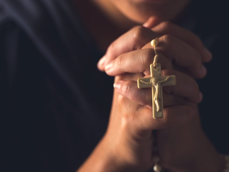 Praying hands clasp rosary 