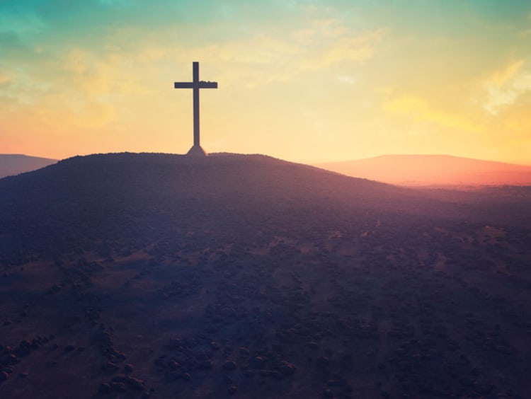 Cross on a hill in front of a sunset