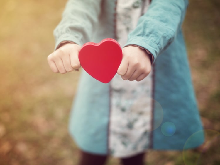 Woman holds out a cutout in the shape of a red heart