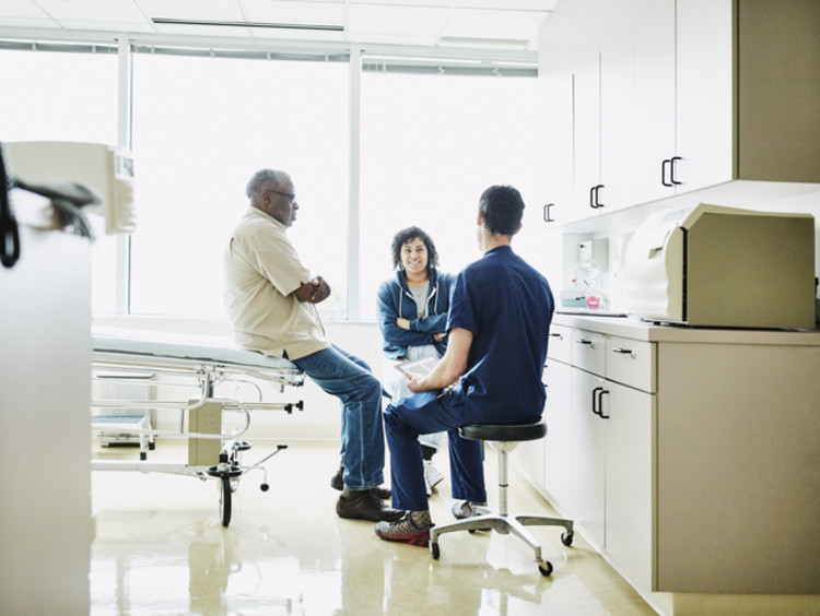 Nurse speaking with man sitting on hospital bed and woman sitting beside bed in hospital room