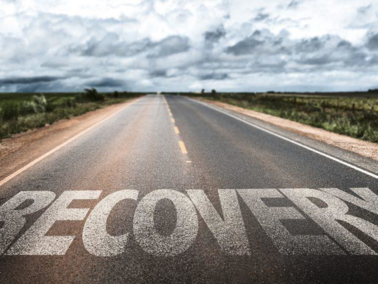 Large letters spell recovery on empty road with a cloudy sky ahead