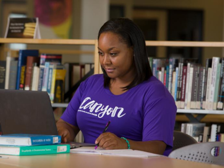 GCU Student in library working on laptop