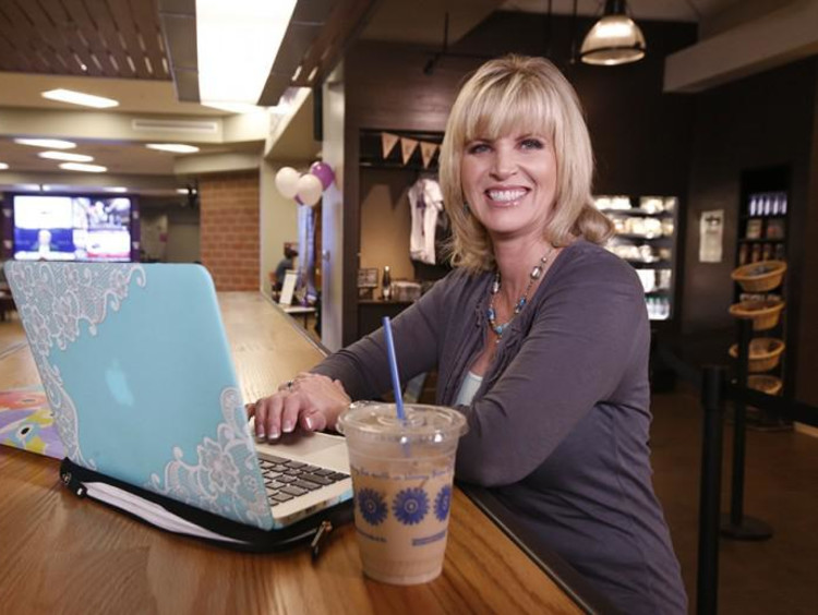 Middle-aged blonde sits a high rise table in a coffee shop