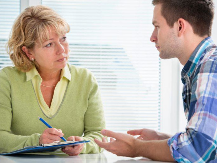 Blonde mental health specialist takes notes of a younger male talking to her