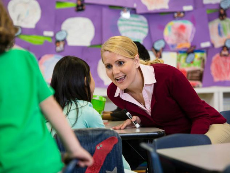 A teacher sits next to a student's desk to talk to them
