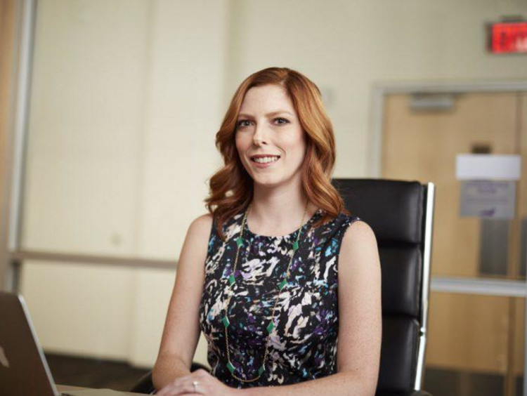Professional woman with red hair sits in office chair with laptop open
