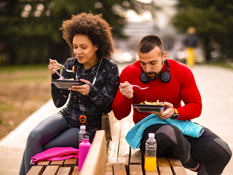Two athletes eating on a bench