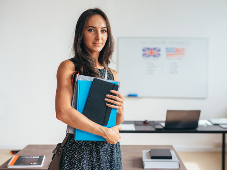 Spanish teacher standing in classroom with books beside whiteboard