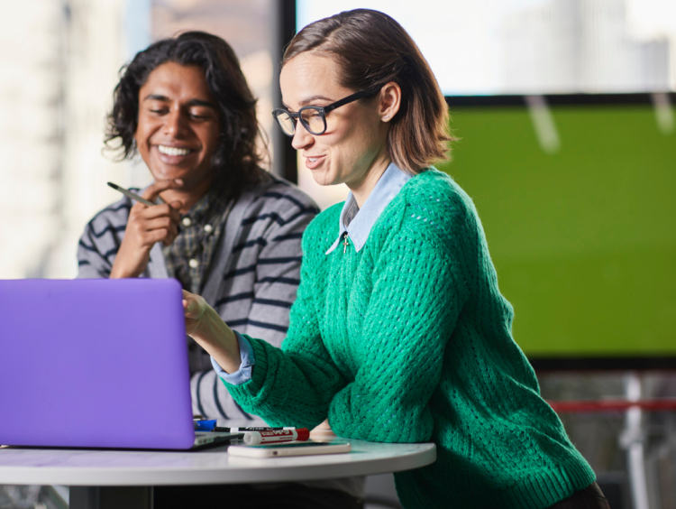 Two students work at laptop in office setting