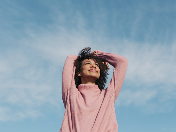 Woman smiles and looks up at the blue sky