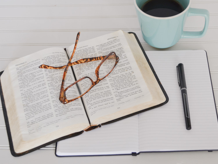 Bible surrounded by notebook, coffee and glasses