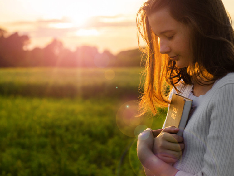 Young woman clutches Bible as the sun sets