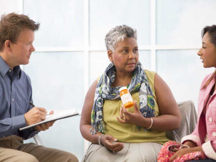 Man takes notes while older woman holds a pill bottle confronting younger teen
