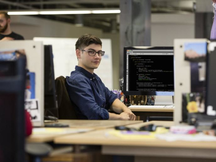 student sitting at computer and smiling at the camera