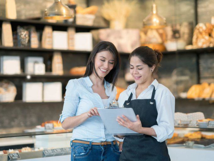 Two businesswomen review a checklist at a chic market shop