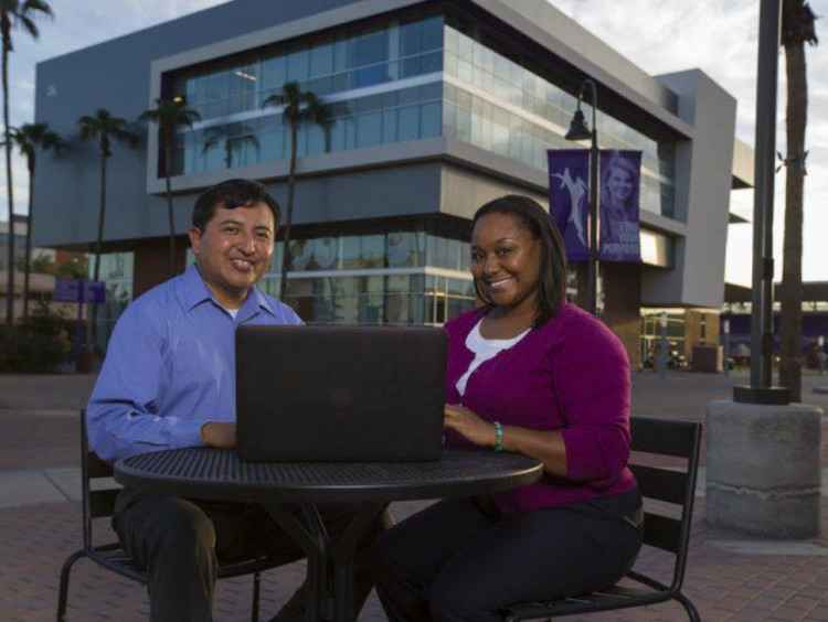 Two adult students sitting on campus in front of the student union