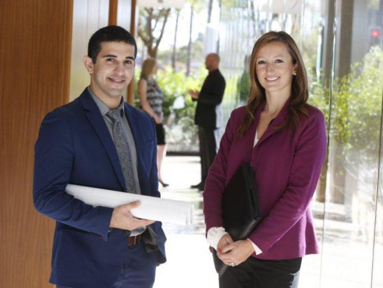 Man holds rolled up blueprints and woman stands next to him