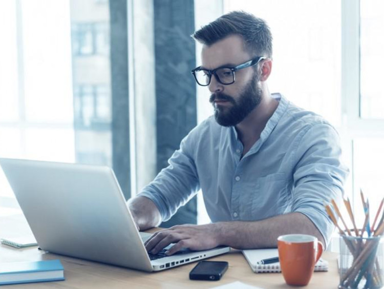 Bearded male sits at desk and uses laptop