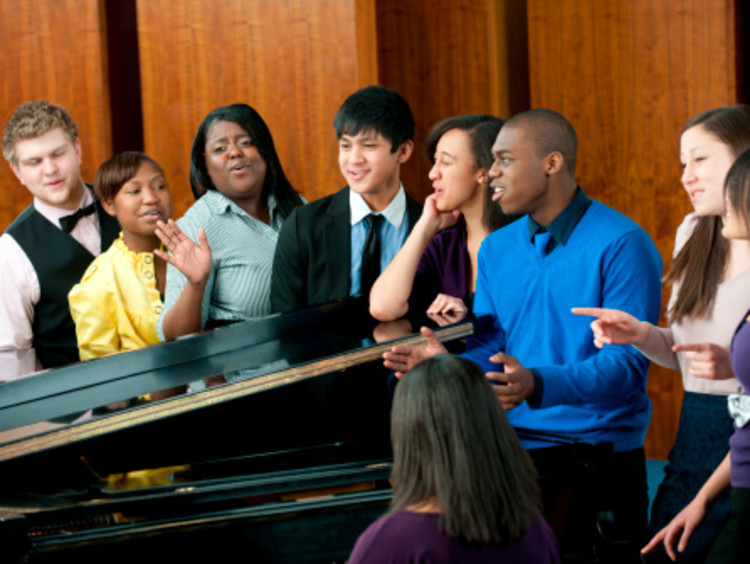 African-American male worship leader in blue shirt leading an interracial choir around a black piano