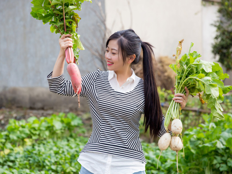 girl in a garden holding up two different vegetables