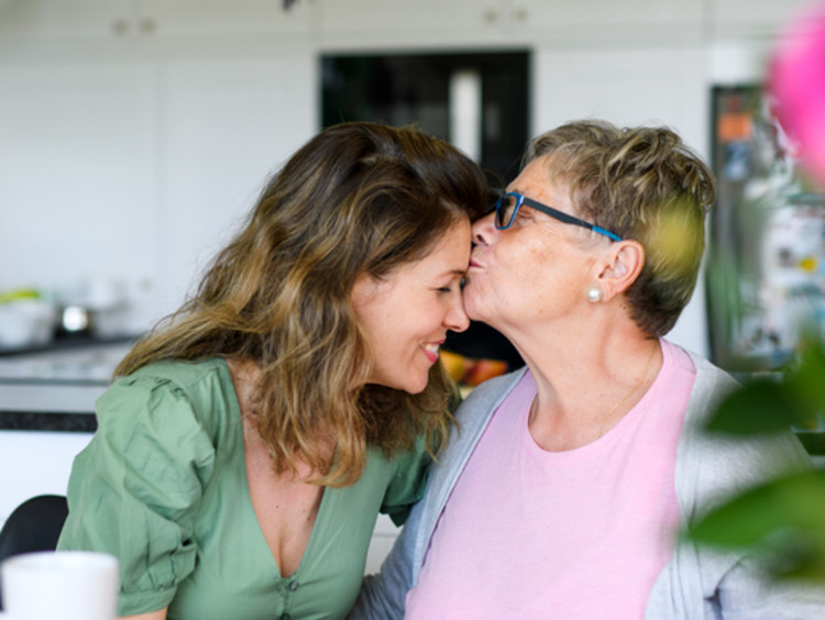 Senior mother kissing adult daughter on her forehead