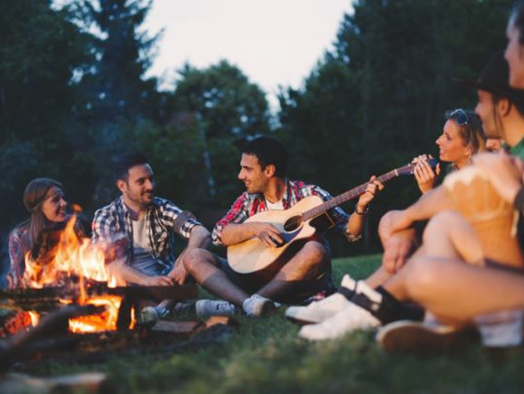 Friends gather and sing around a camp fire