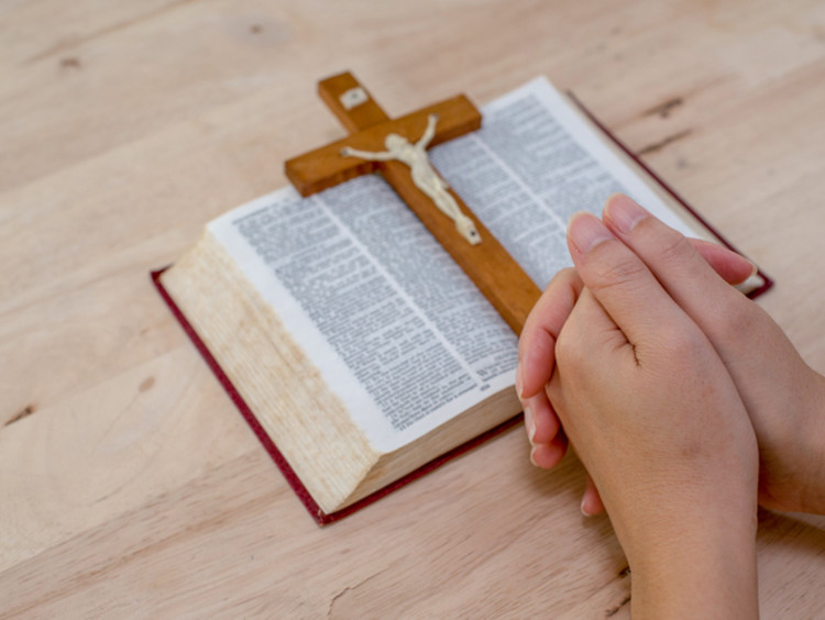 Praying hands are accompanied by a cross and Bible