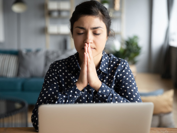 Woman in blue and white polka dot button-down shirt praying at work