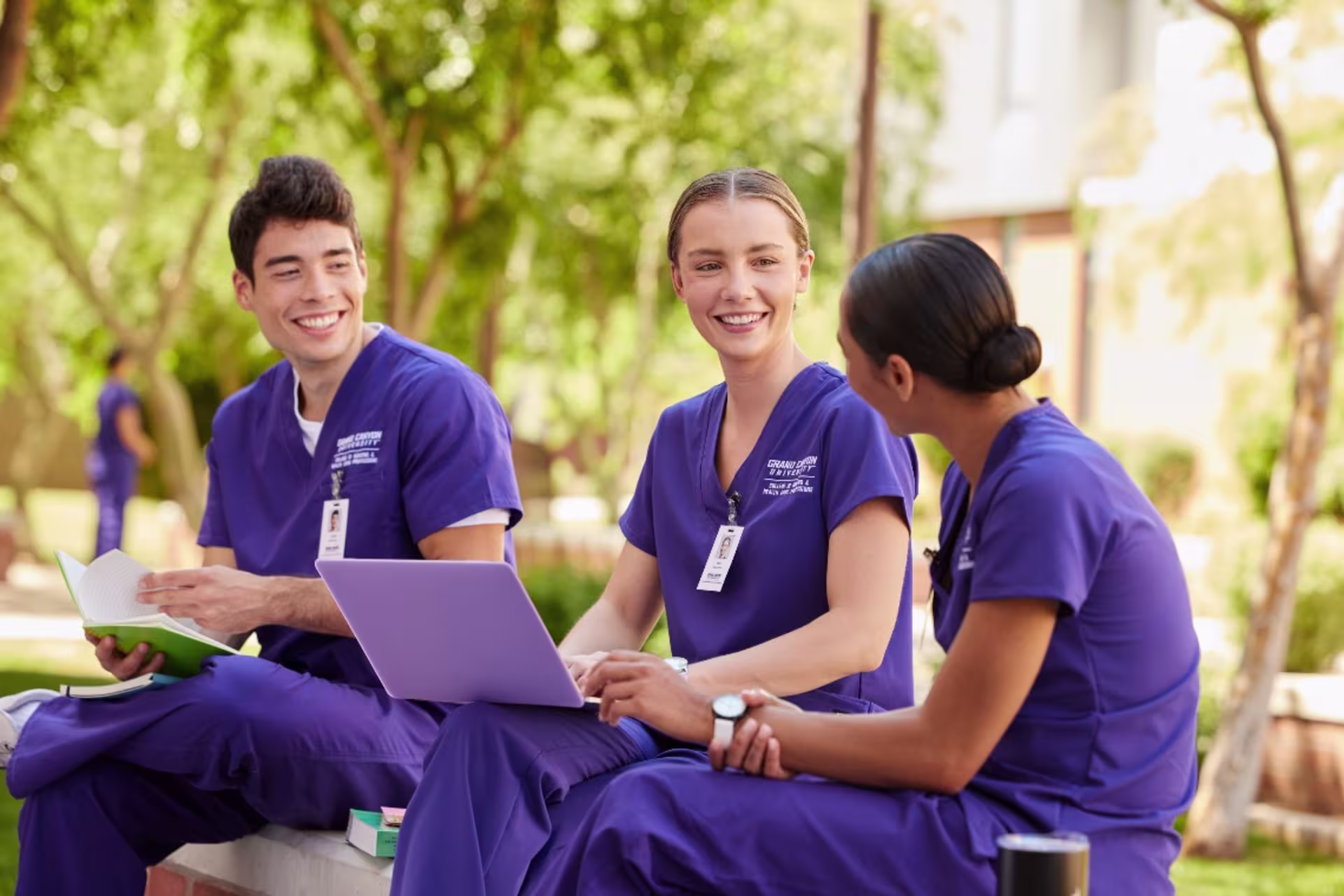 3 nurses sitting outside in purple scrubs and studying