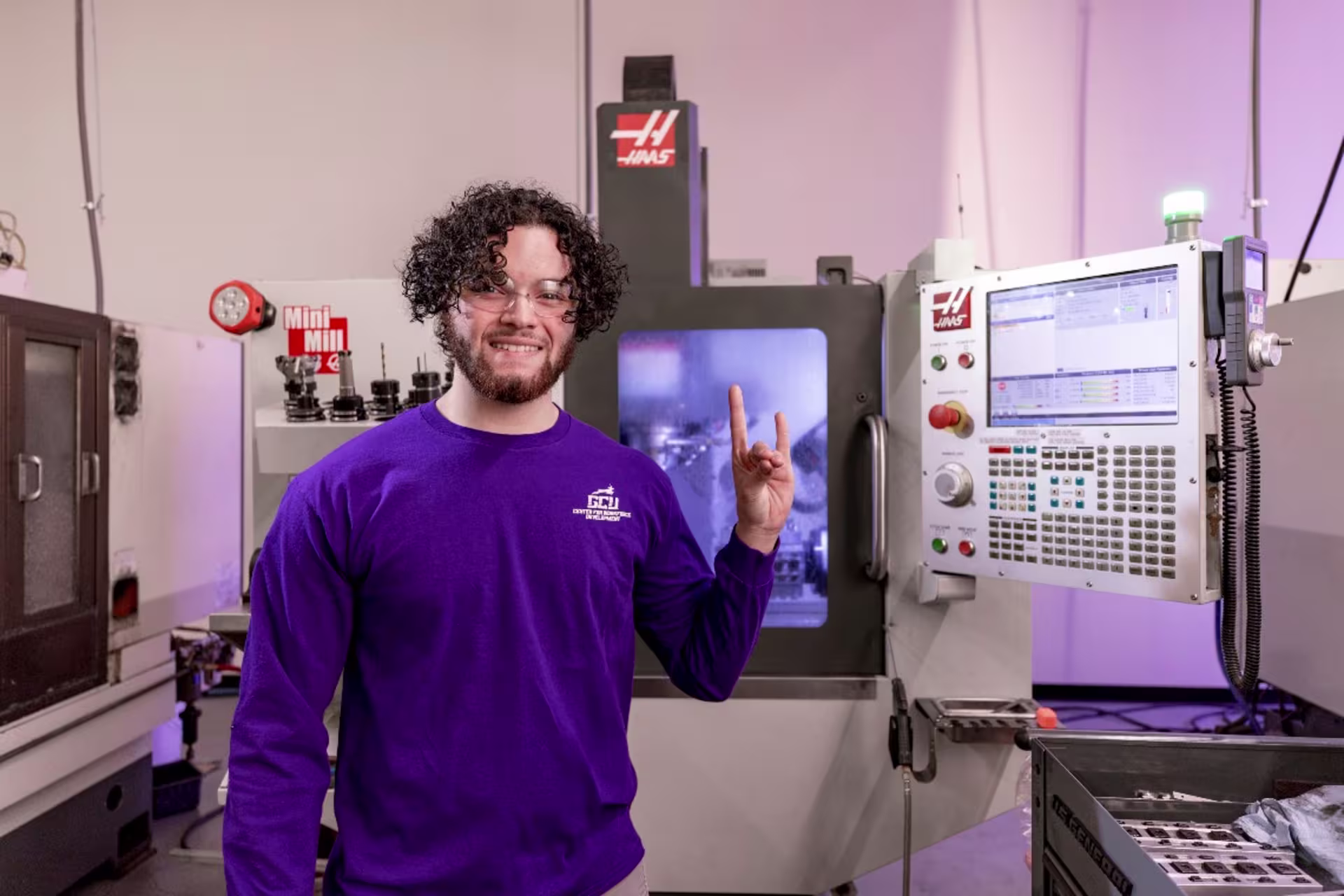 Engineering student in purple shirt standing in lab throwing lopes hand sign