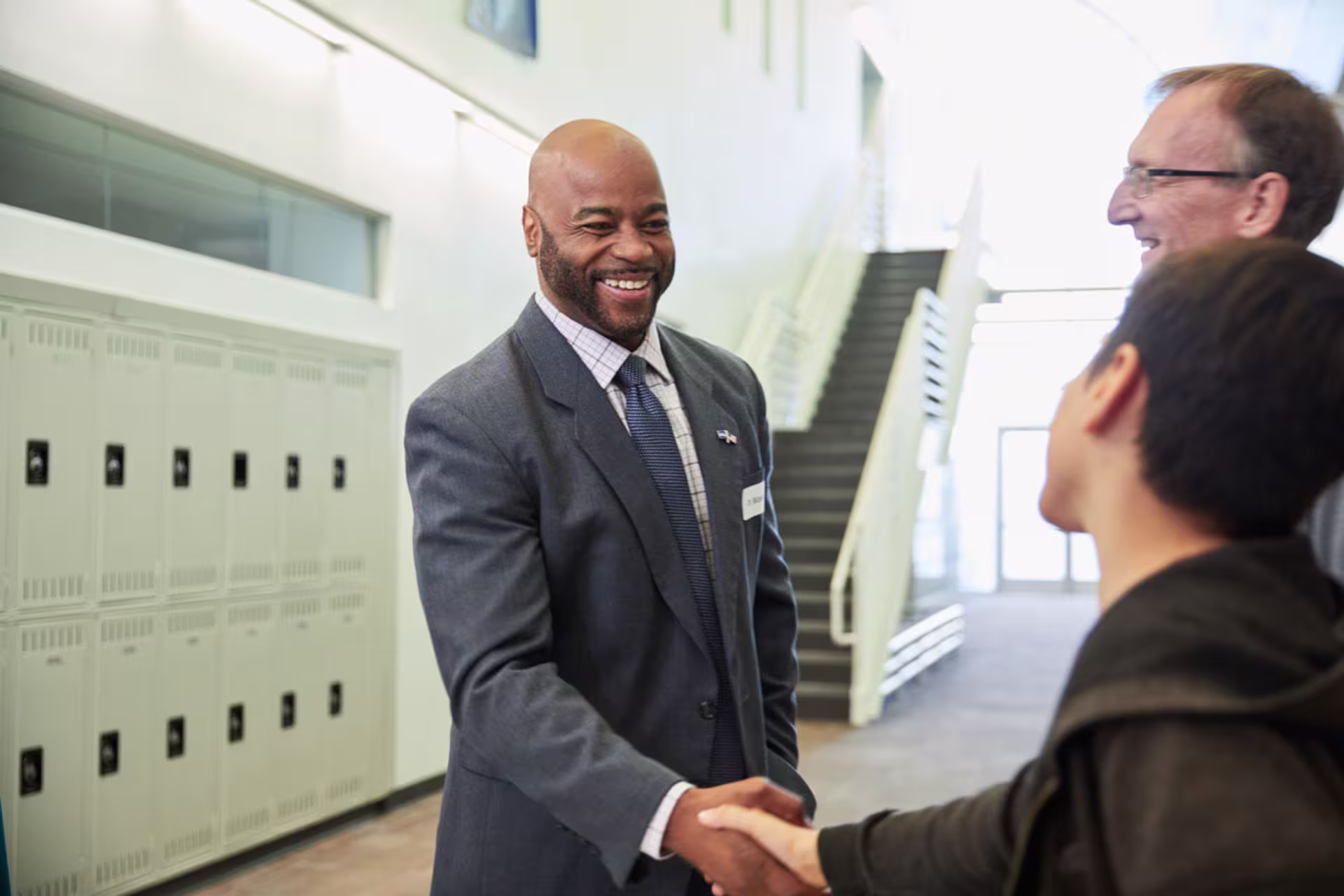 Male CDS professional shaking hands with young male student in hallway with male educator beside them