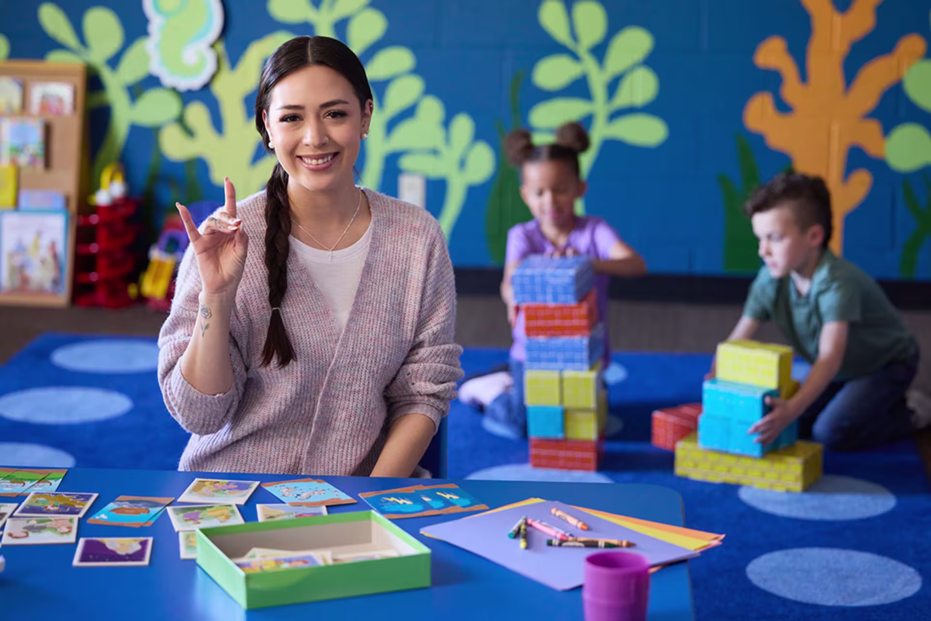 Female early childhood education teacher smiling with young students playing in background