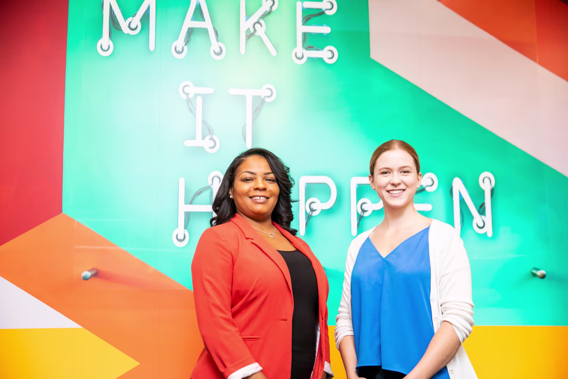 Two female life coaches smiling in front of bright painted wall