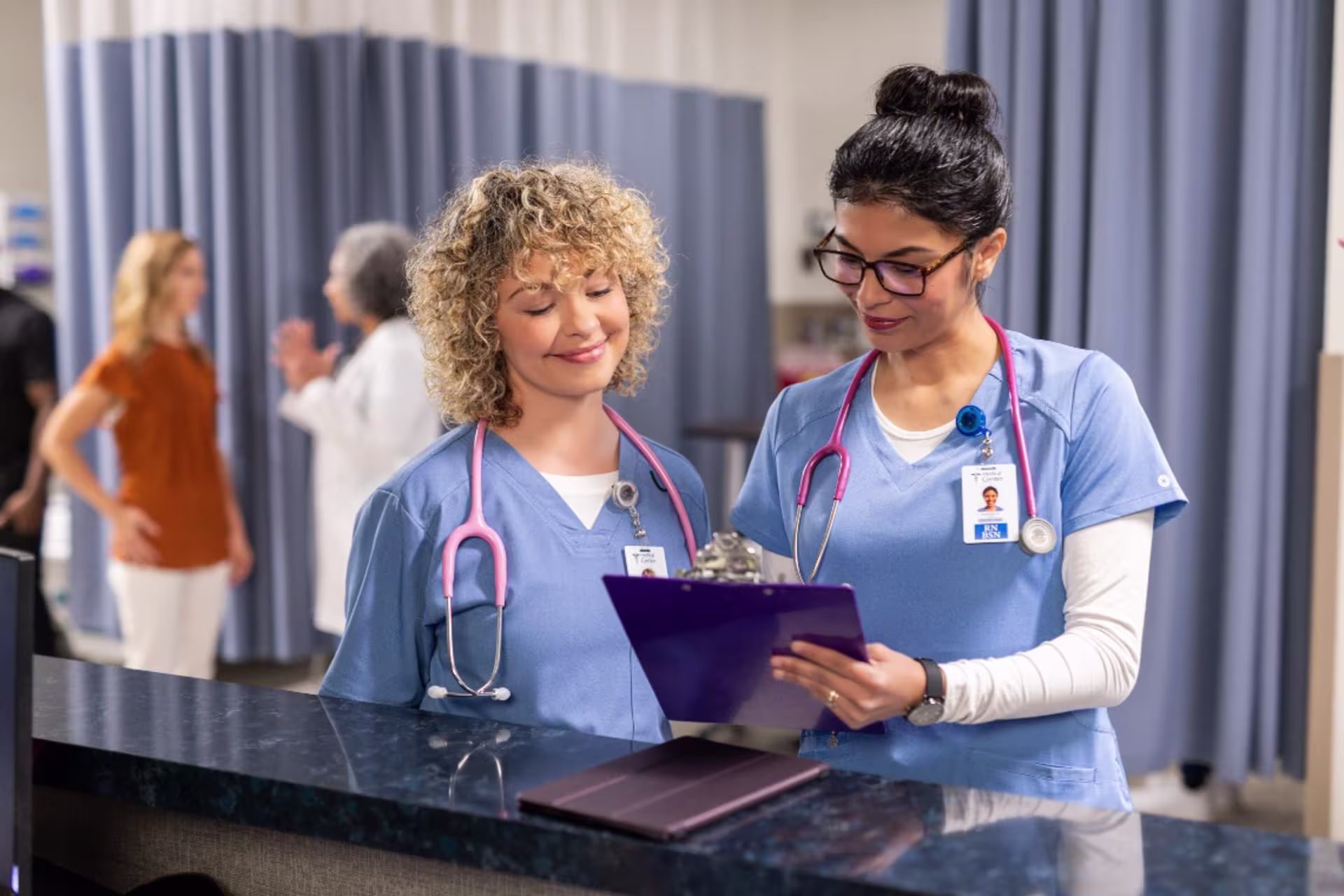 Two nurses in blue scrubs reviewing charts in a hospital setting