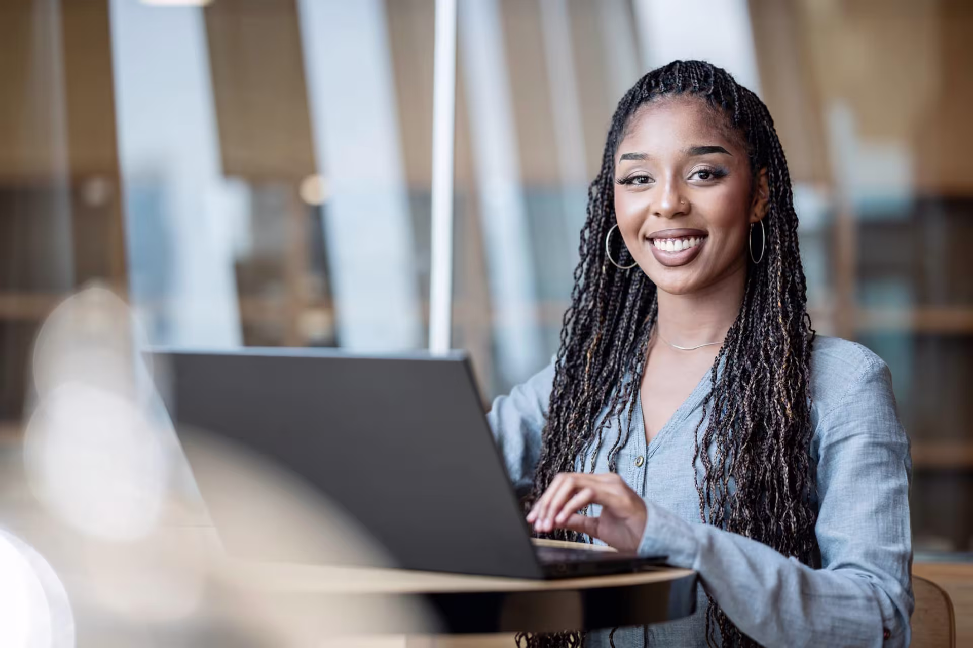 A smiling woman working on a laptop in a modern setting, representing the skills she's learning through an MBA in Accounting program.
