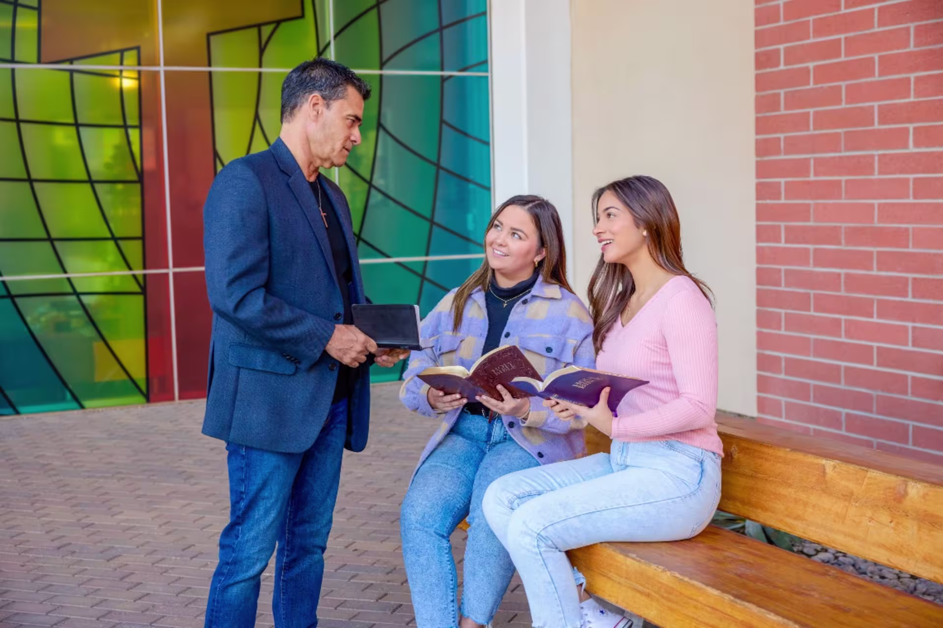 Man with two female teens reading the bible outside on a bench