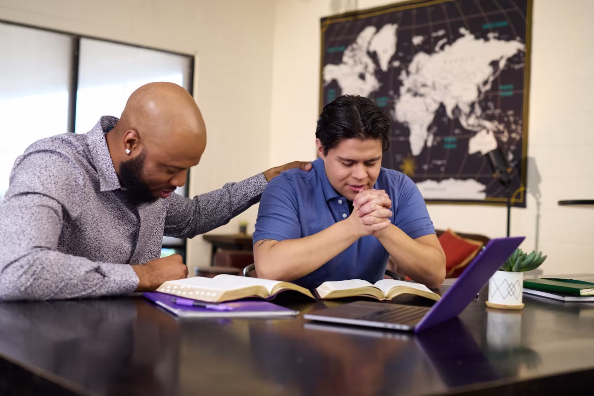 Young man sitting at a table with a bible and praying with a teacher