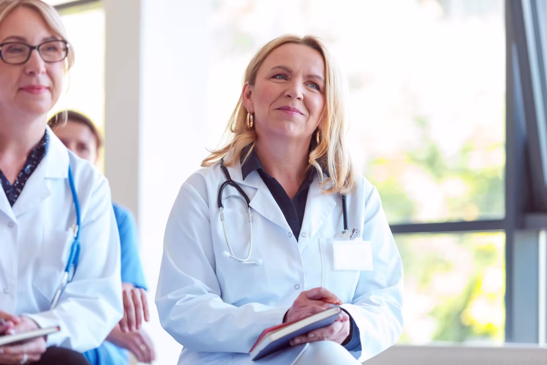 Healthcare professionals in a learning environment, with a confident nurse leader taking notes, representing DNP in educational leadership.