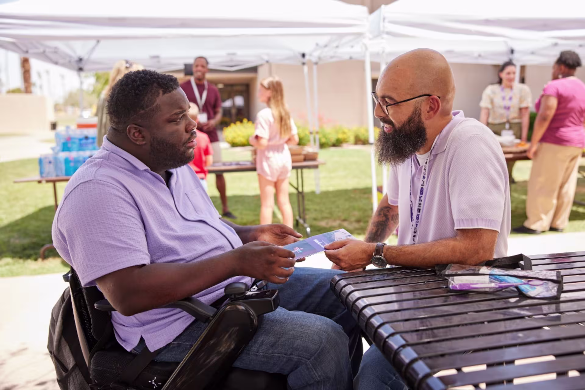 Counselor sitting outside and handing a man in a wheelchair a pamphlet