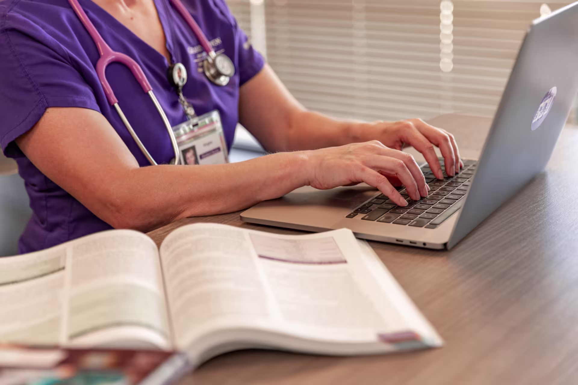 white female nursing student with open textbook does online classwork