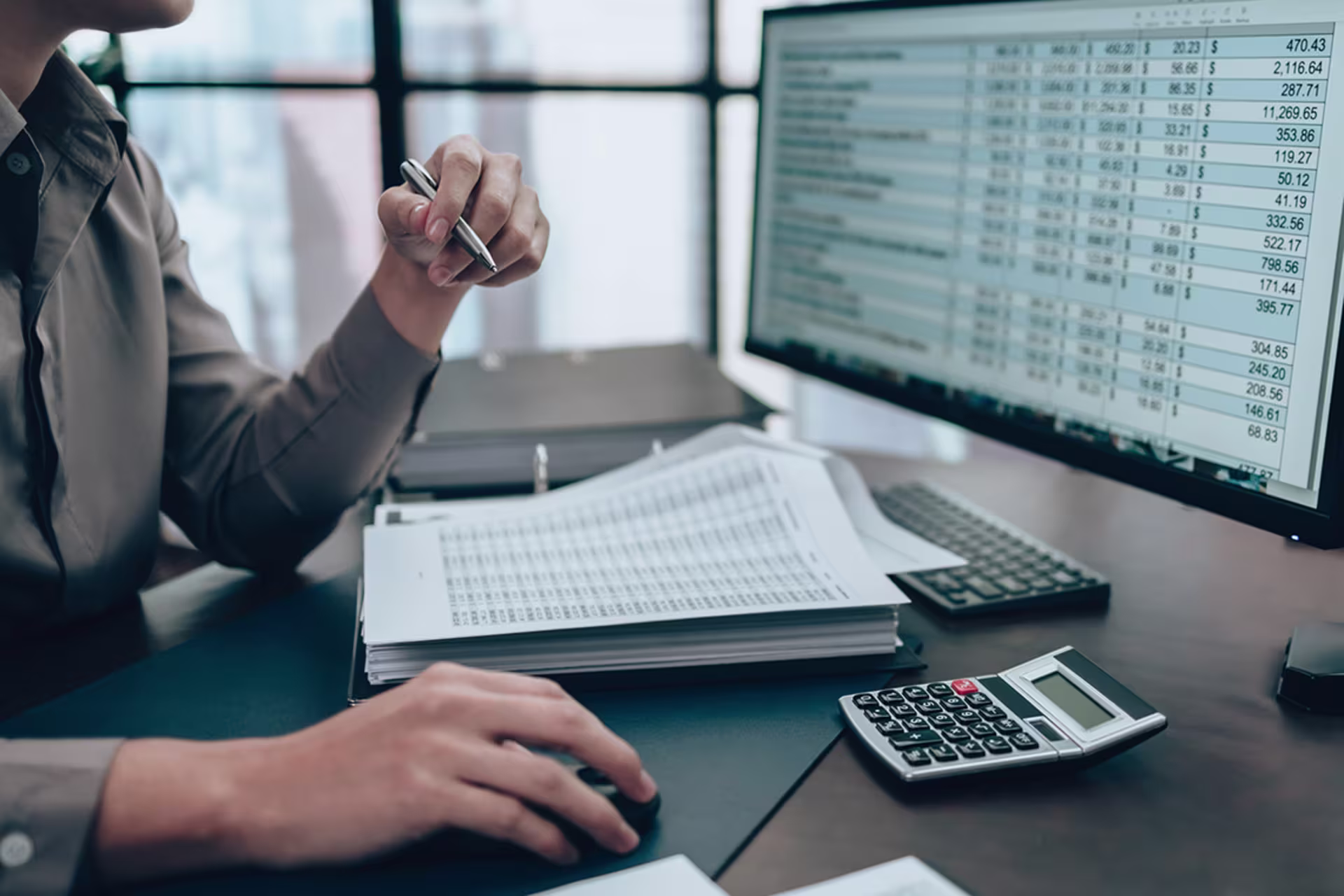 man in brown button-down reviewing accounting ledger on computer
