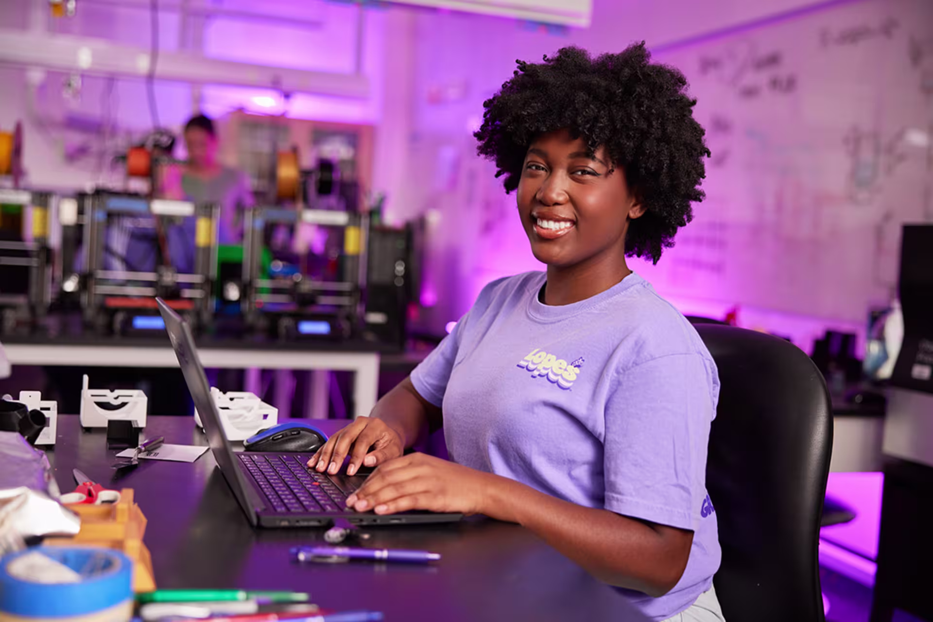 black girl with great fro in light purple shirt types on black laptop