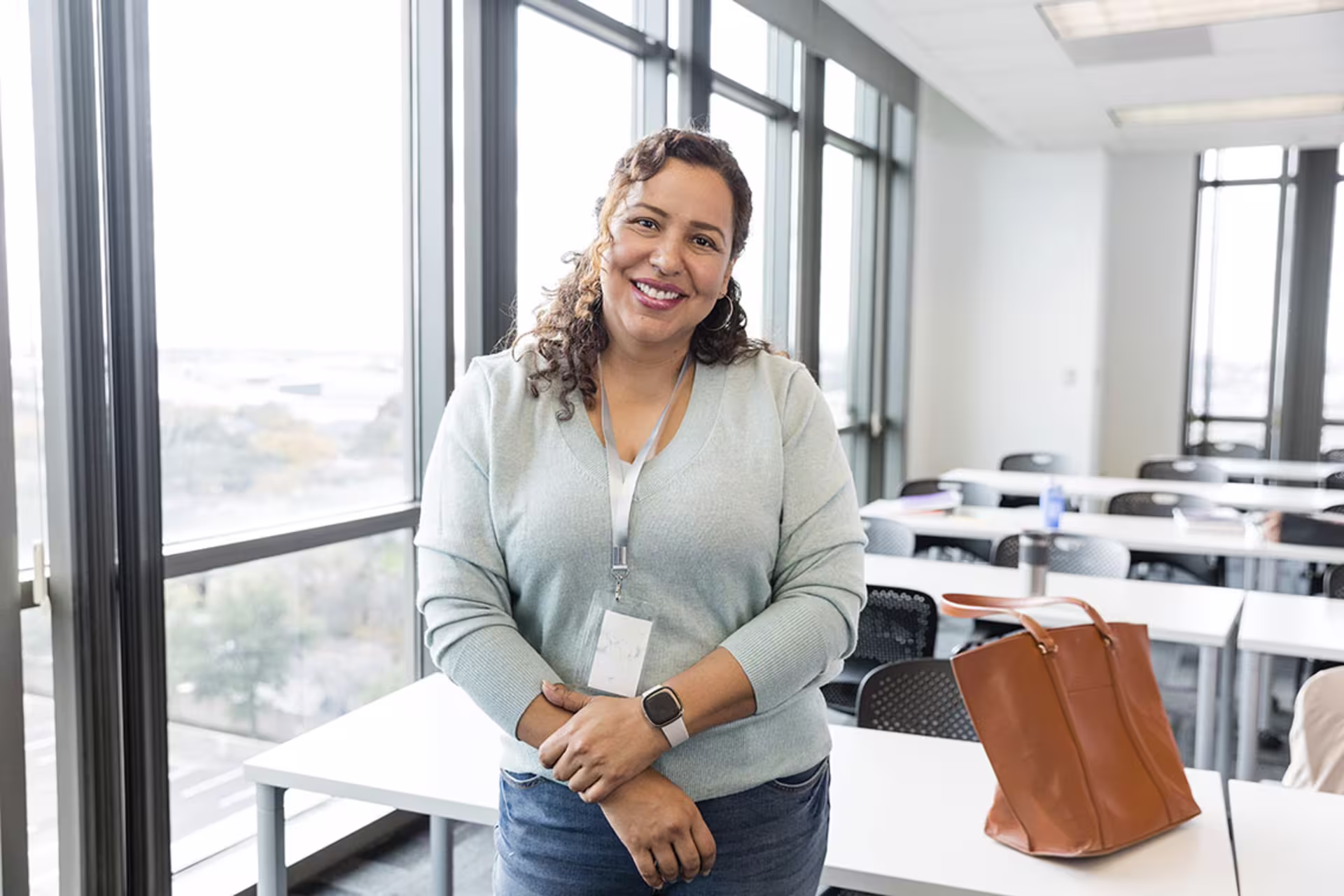 Female adult learning professor leaning against classroom table and smiling at camera