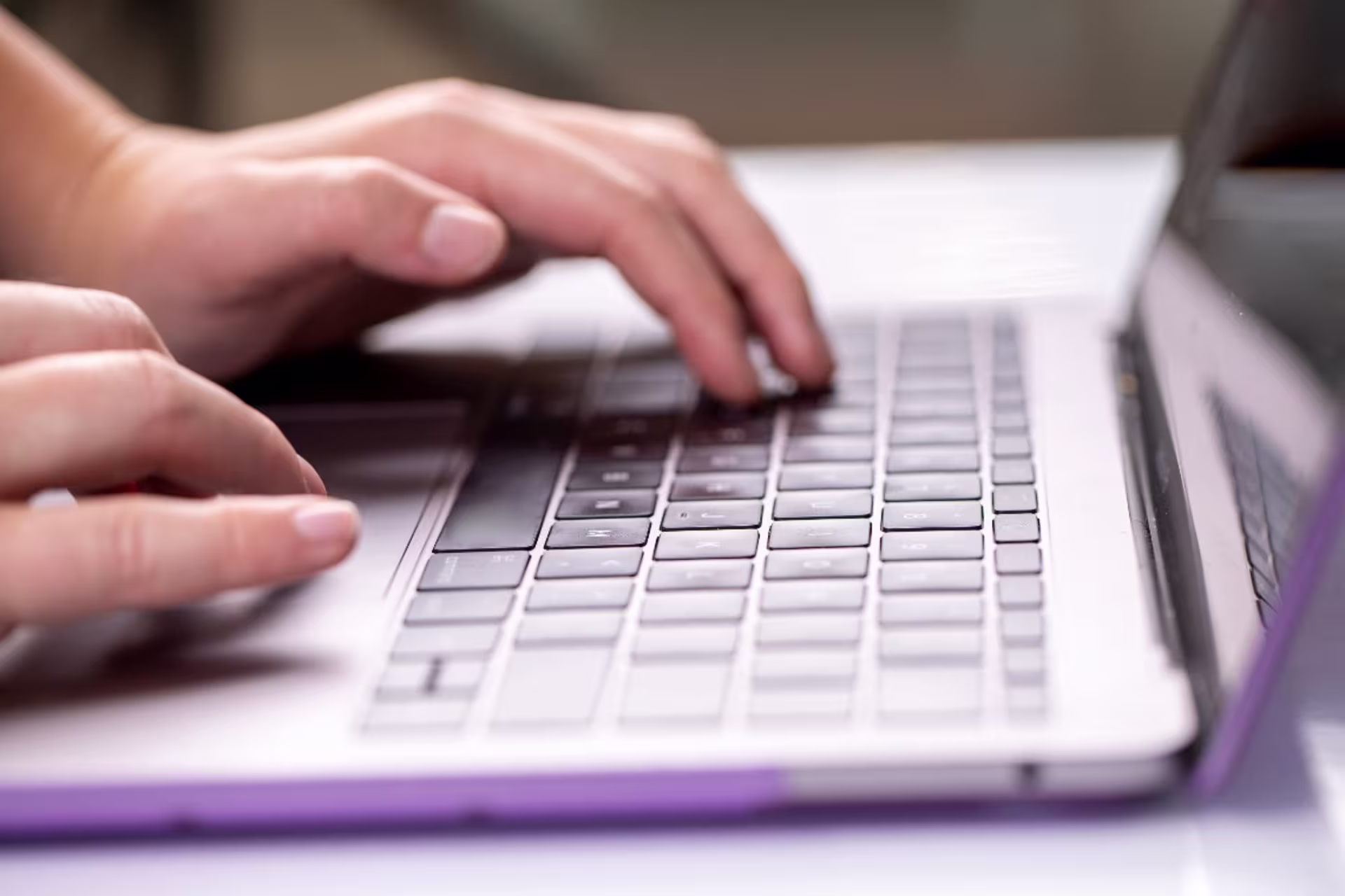 Close up of hands typing on an open laptop with a purple case