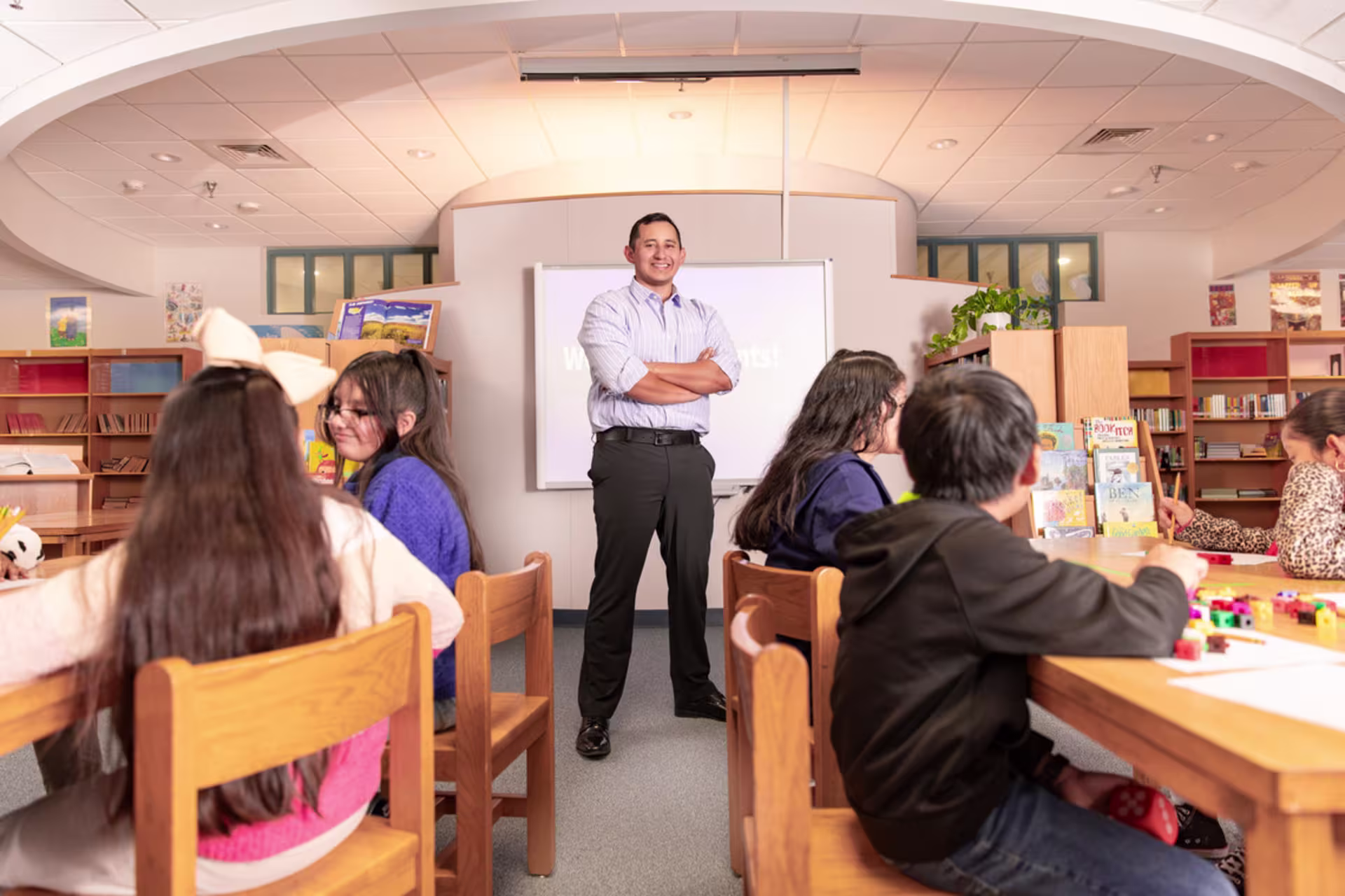 hispanic male principal stands authoritatively in elementary classroom