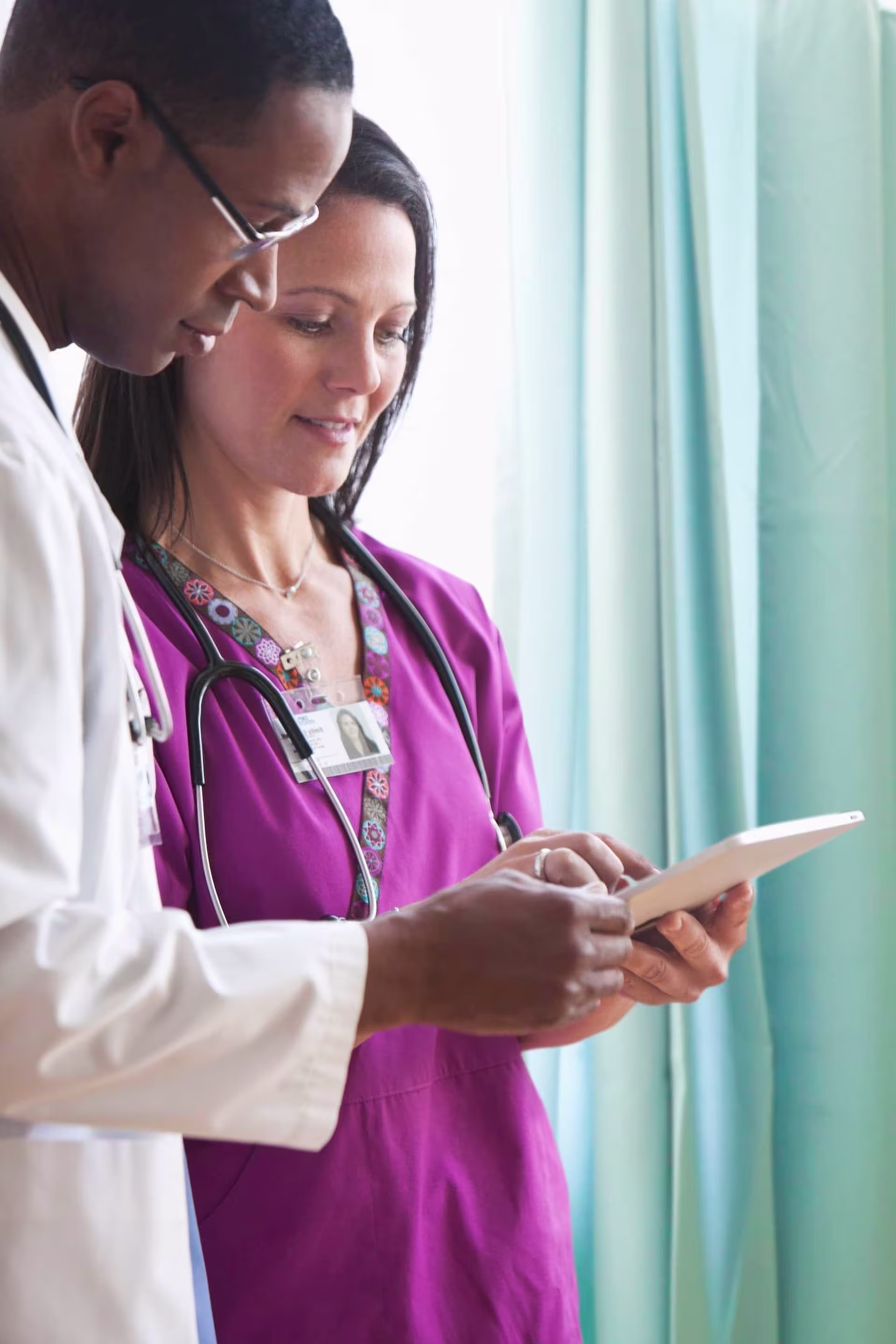 Physician assistant consulting with a doctor while reviewing patient information on a tablet.