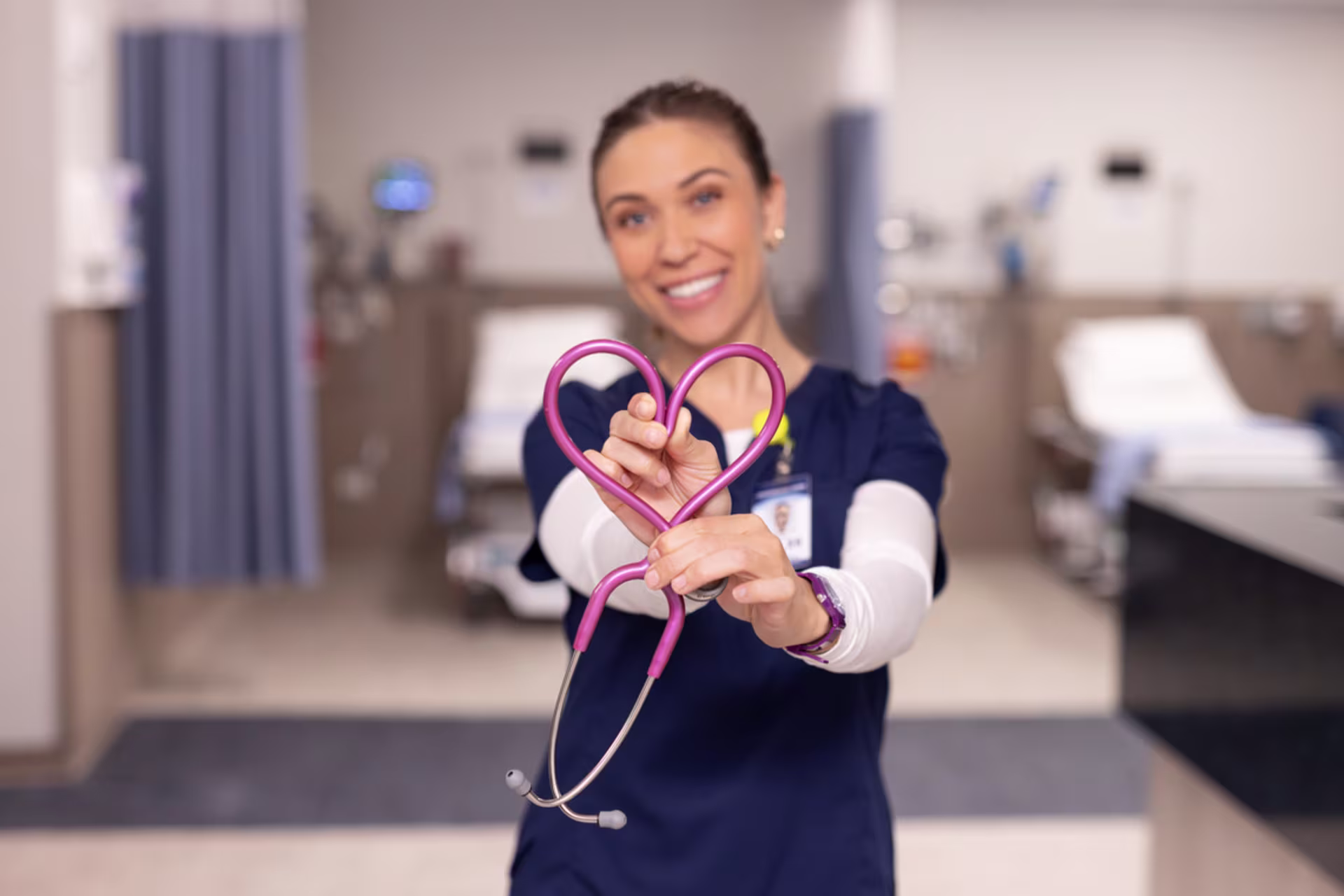 white female nurse makes heart shape with stethoscope in empty hospital room